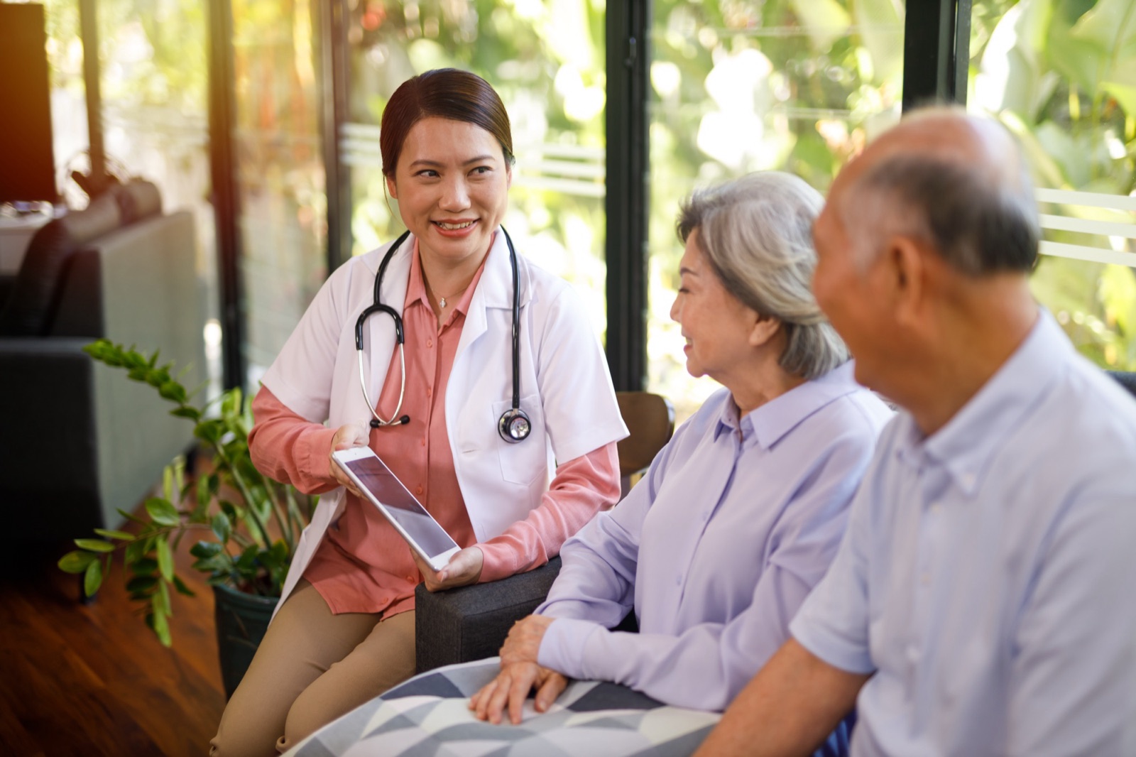 A health professional in a white coat going through notes on a tablet with an older couple at home