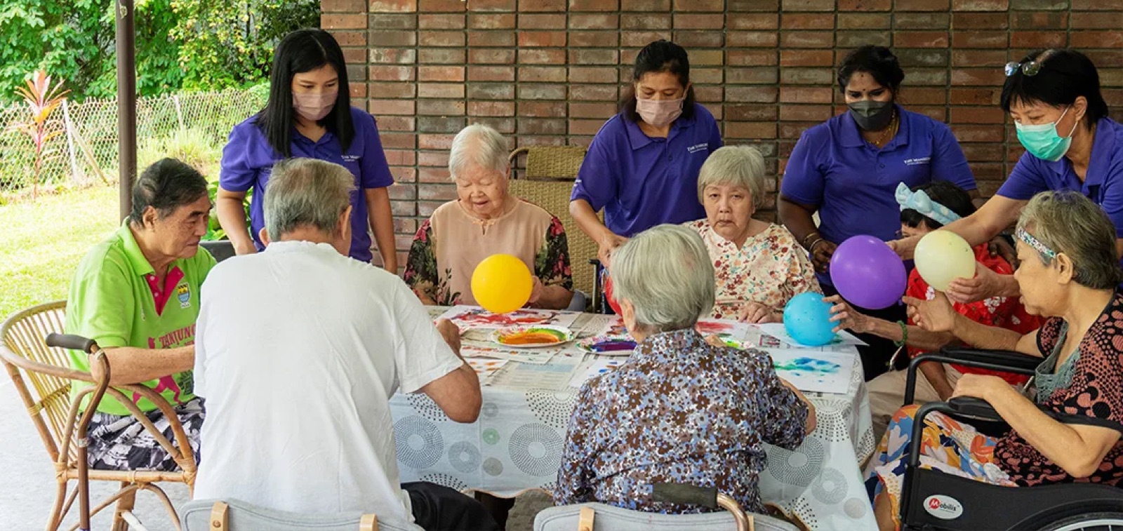 Residents and caregivers playing a balloon game around a table at a residence