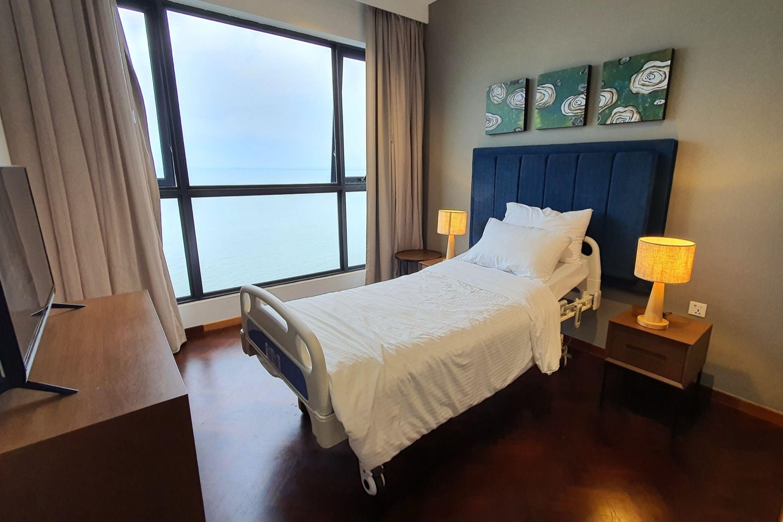 A care suite at Tanjung Point Residences with an adjustable bed, bedside lamps and a large window looking out to sea