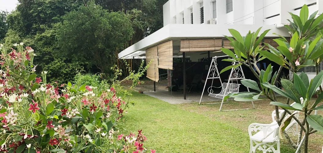 A garden lawn with flowering shrubs, a swing bench and a covered patio beside a white house