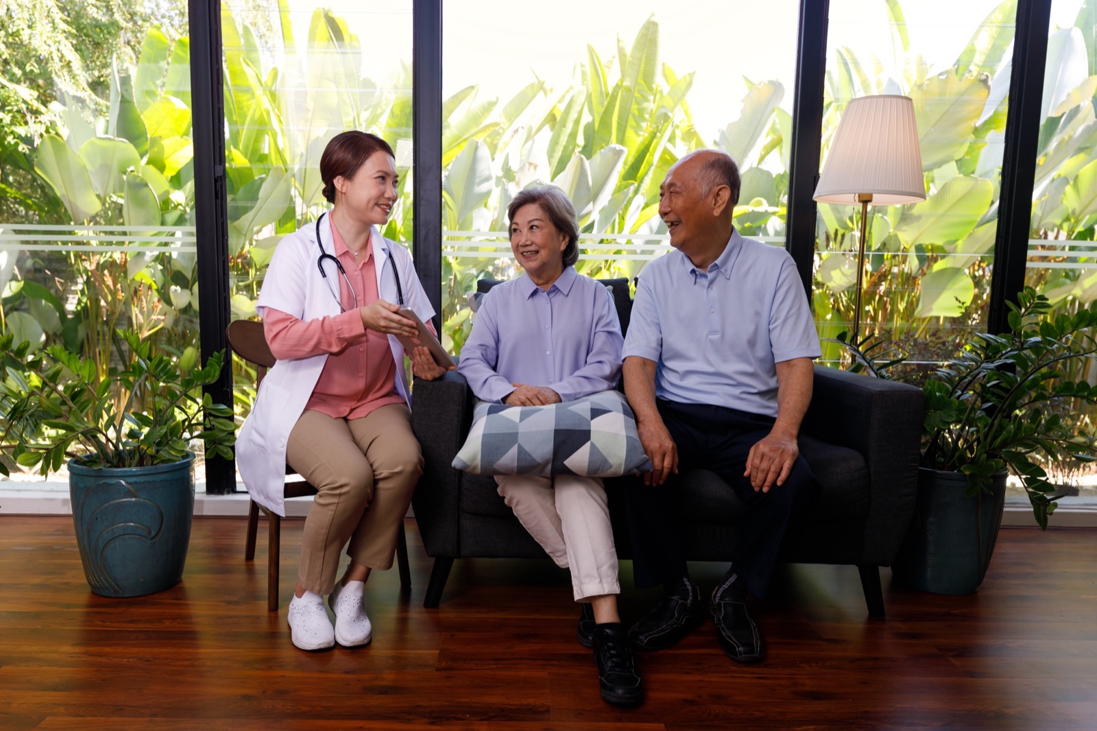 A doctor talks with an older couple sitting on a sofa at home